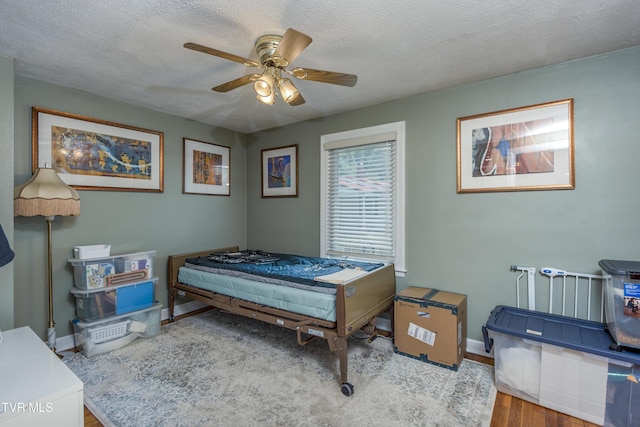 bedroom with ceiling fan, a textured ceiling, baseboards, and wood finished floors