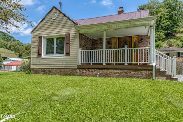 back of property with metal roof, brick siding, a yard, and a chimney