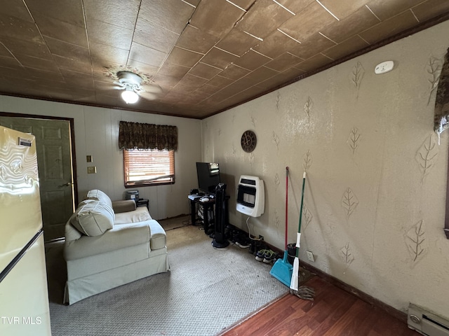 living area with heating unit, wood finished floors, baseboards, a textured wall, and baseboard heating