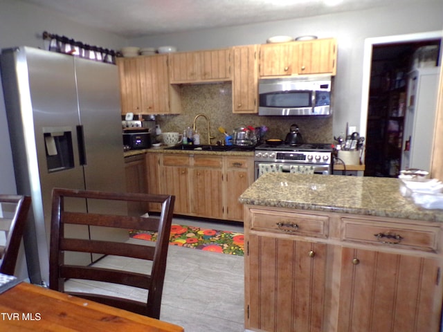 kitchen featuring a sink, light stone counters, backsplash, and appliances with stainless steel finishes