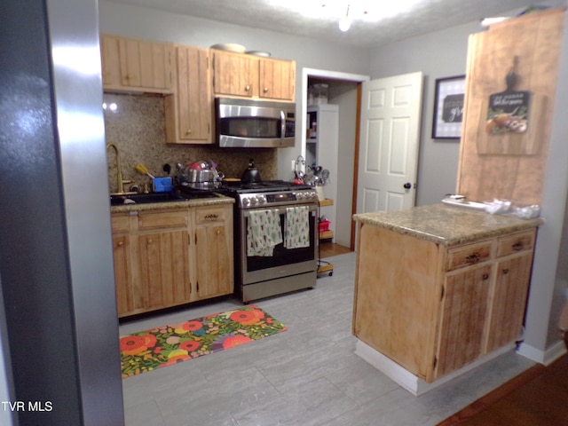 kitchen with a peninsula, a sink, decorative backsplash, light brown cabinetry, and stainless steel appliances