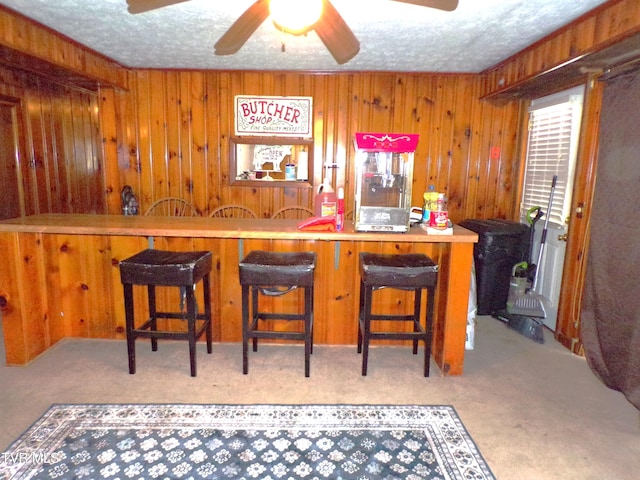 bar with indoor wet bar, wooden walls, a textured ceiling, and ceiling fan