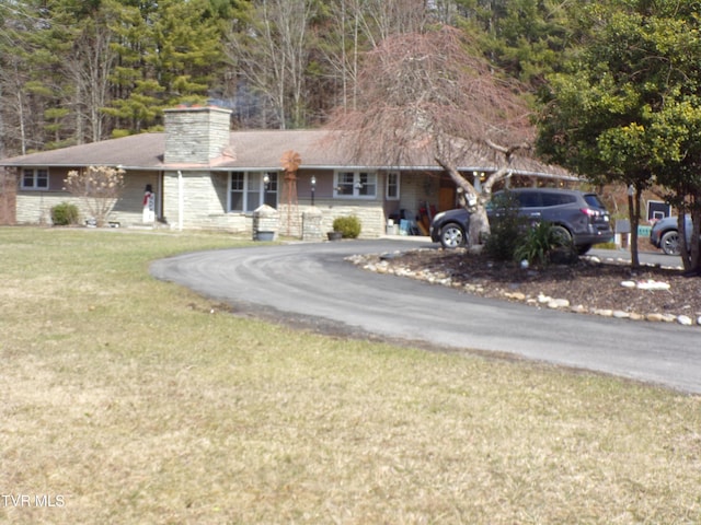 ranch-style house featuring aphalt driveway, a front yard, stone siding, and a chimney