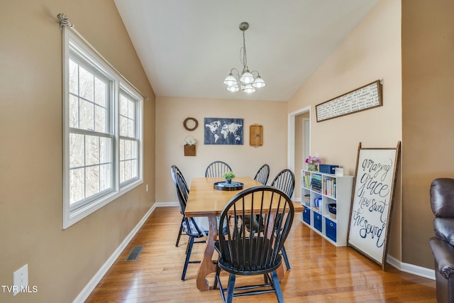 dining space featuring visible vents, baseboards, a chandelier, lofted ceiling, and light wood-style floors