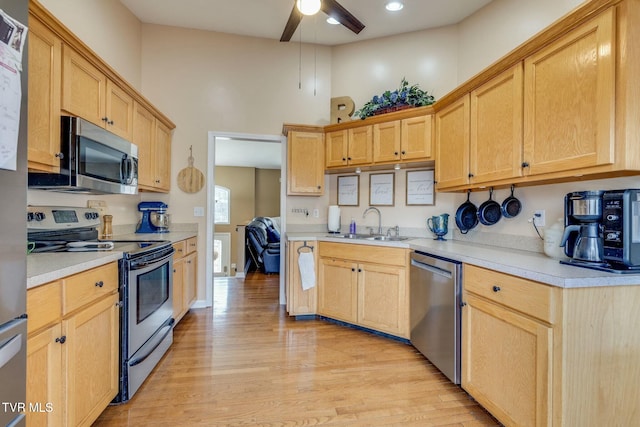 kitchen with light wood finished floors, a high ceiling, light brown cabinetry, light countertops, and appliances with stainless steel finishes