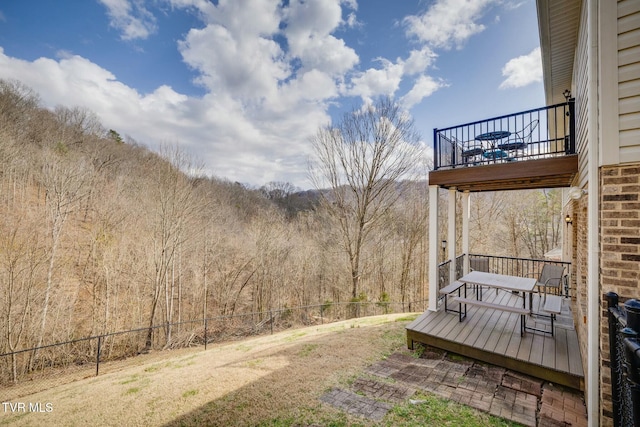 view of yard with a forest view, a balcony, and fence