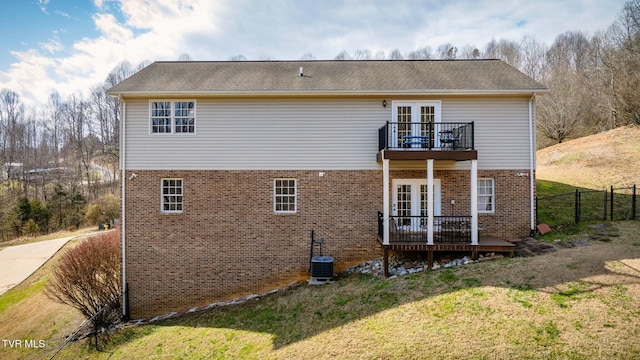 rear view of house featuring fence, a yard, french doors, a balcony, and brick siding