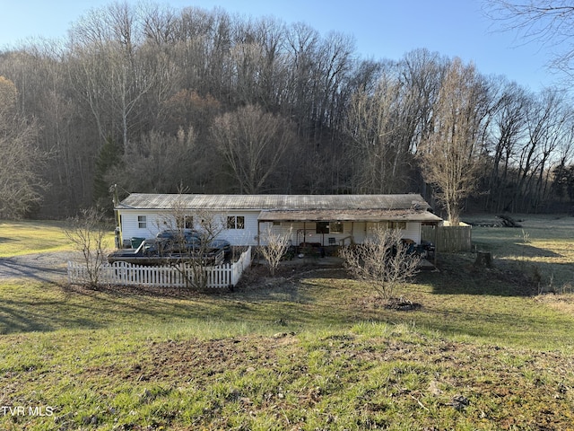 view of front facade featuring a wooded view, a front lawn, and fence