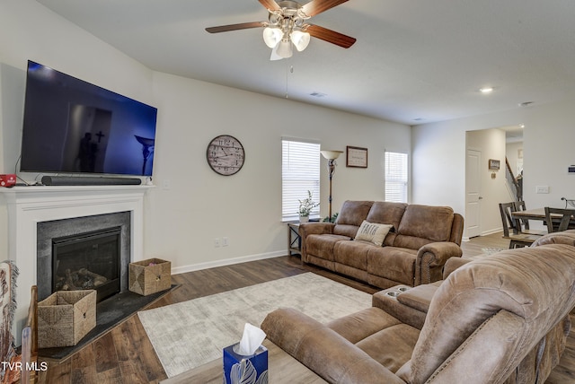 living area with baseboards, wood finished floors, a glass covered fireplace, and a ceiling fan