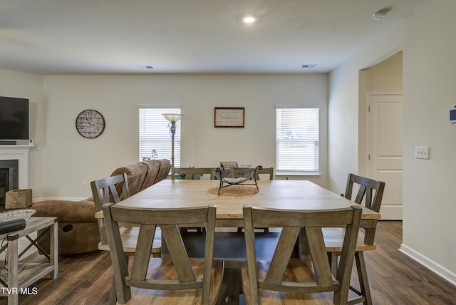 dining area featuring a glass covered fireplace, dark wood finished floors, visible vents, and a wealth of natural light