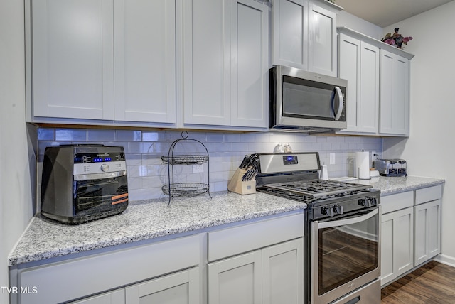 kitchen featuring dark wood-style floors, backsplash, stainless steel appliances, and light stone countertops