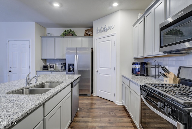 kitchen featuring light stone countertops, recessed lighting, dark wood-style floors, stainless steel appliances, and a sink