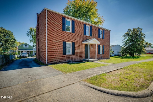 view of front facade featuring aphalt driveway, brick siding, a front lawn, and fence