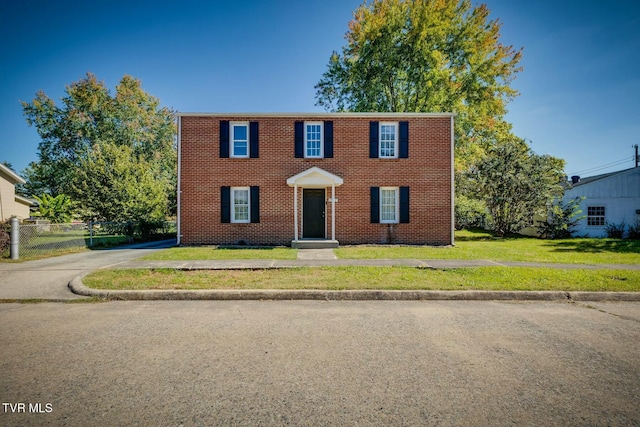 colonial inspired home featuring a front lawn, fence, brick siding, and driveway