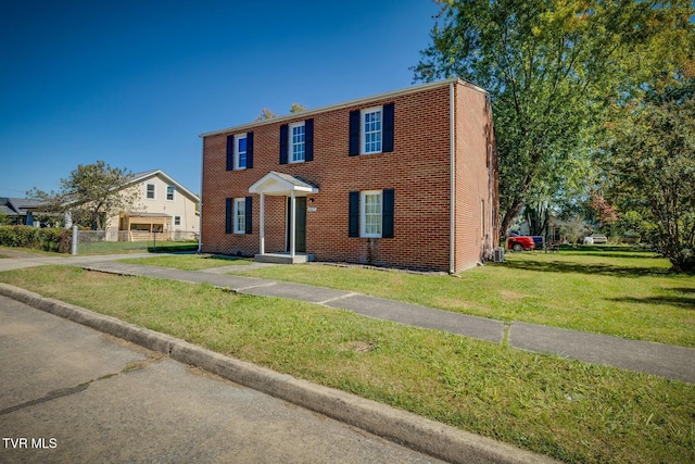 colonial home featuring brick siding, a front lawn, and fence