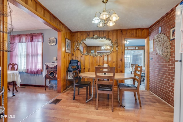 dining area featuring wood walls, visible vents, brick wall, and a chandelier