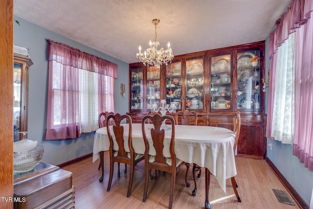 dining area with light wood finished floors, visible vents, baseboards, and a notable chandelier