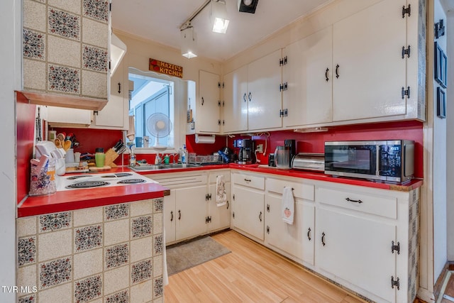 kitchen featuring light wood-type flooring, stainless steel microwave, rail lighting, and white cabinetry