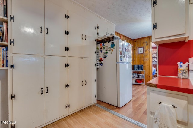 kitchen with a textured ceiling, white cabinetry, freestanding refrigerator, wood walls, and light wood finished floors