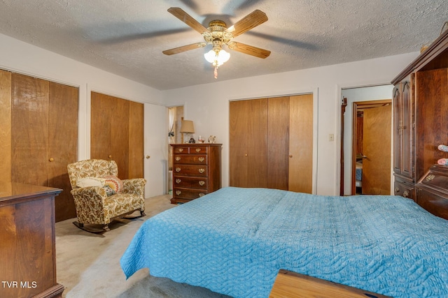 carpeted bedroom featuring ceiling fan, two closets, and a textured ceiling