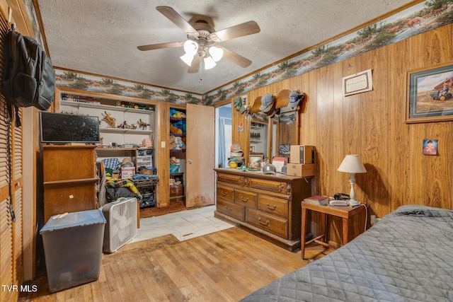 bedroom with a textured ceiling, wood finished floors, a ceiling fan, and wood walls