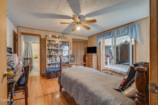 bedroom with wooden walls, a ceiling fan, light wood-style floors, a textured ceiling, and access to outside