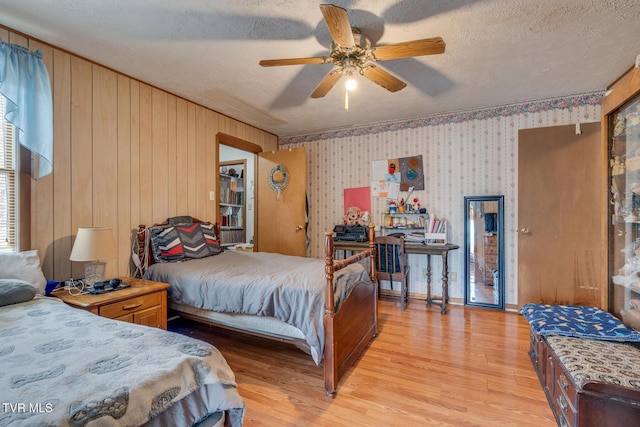 bedroom featuring a textured ceiling, light wood-style floors, ceiling fan, and wallpapered walls