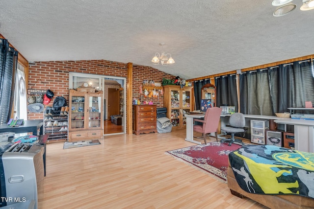 home office featuring brick wall, vaulted ceiling, wood finished floors, a notable chandelier, and a textured ceiling