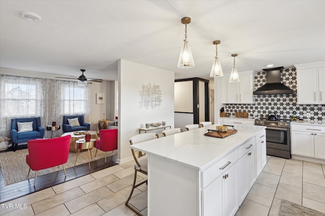 kitchen with open floor plan, stainless steel electric stove, white cabinetry, and wall chimney range hood