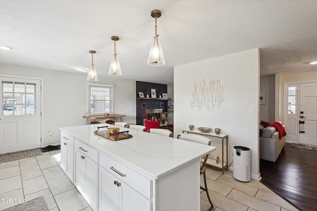 kitchen featuring a brick fireplace, a center island, a breakfast bar area, hanging light fixtures, and white cabinetry