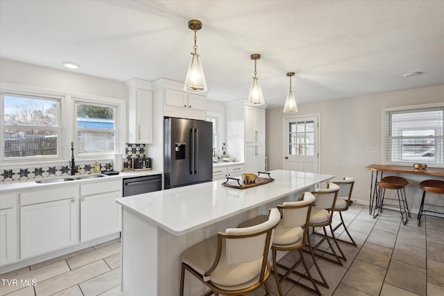 kitchen featuring a breakfast bar, stainless steel refrigerator with ice dispenser, a sink, dishwashing machine, and a healthy amount of sunlight