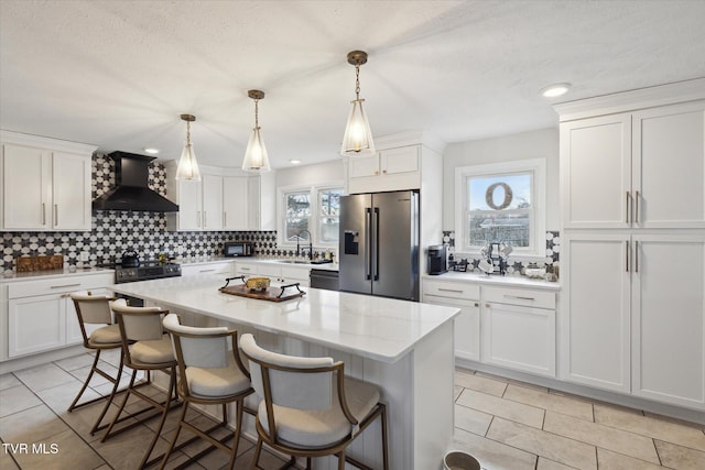 kitchen featuring backsplash, wall chimney exhaust hood, stainless steel refrigerator with ice dispenser, and white cabinetry