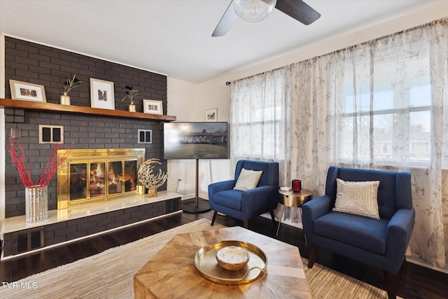 living area featuring a brick fireplace, a ceiling fan, and wood finished floors