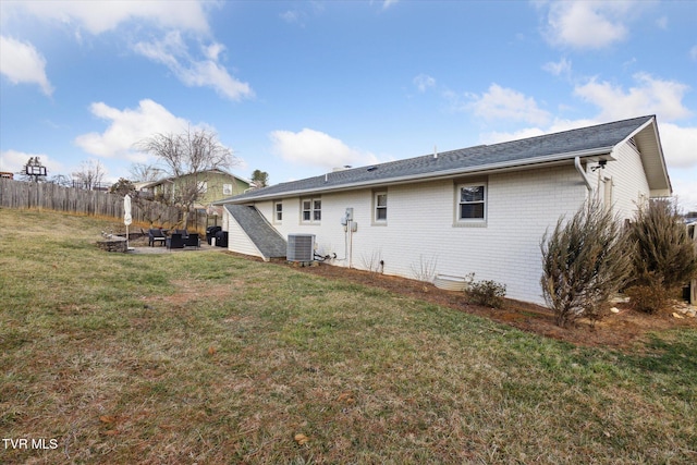 back of property featuring central air condition unit, fence, brick siding, and a lawn