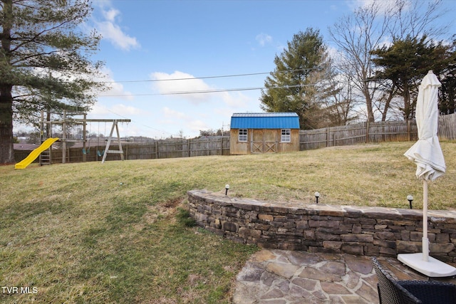 view of yard with a storage unit, an outbuilding, a fenced backyard, and a playground