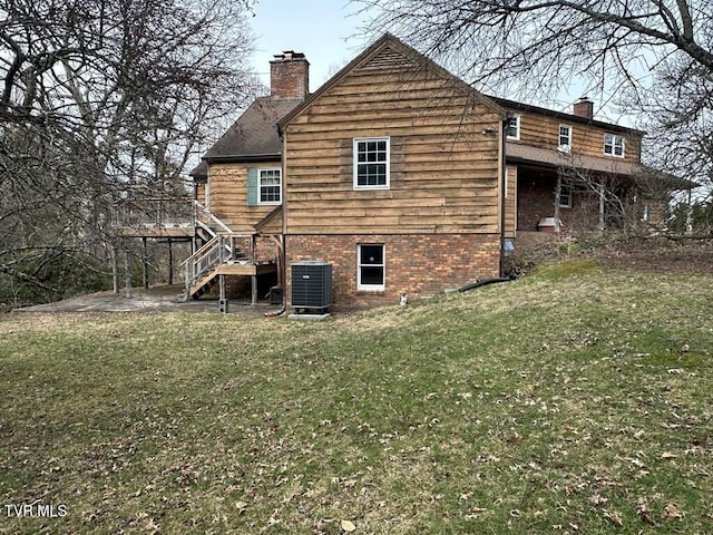 back of property with a lawn, stairs, brick siding, central AC unit, and a chimney