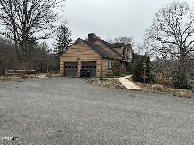 view of home's exterior with aphalt driveway, a chimney, and an attached garage