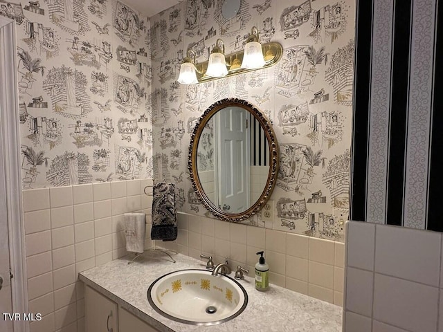 bathroom featuring vanity, tile walls, wainscoting, and wallpapered walls