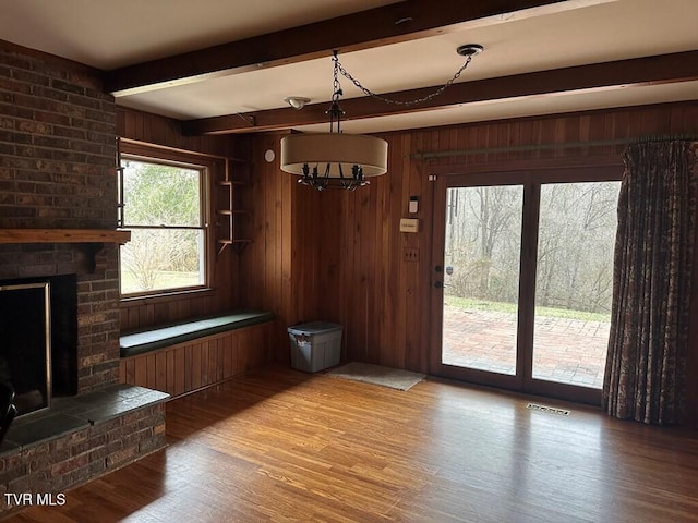 unfurnished dining area with wood finished floors, visible vents, beam ceiling, a fireplace, and wood walls
