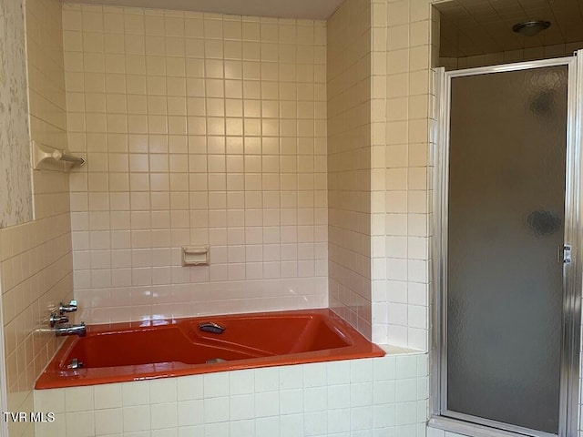 full bathroom featuring tiled bath and a shower stall