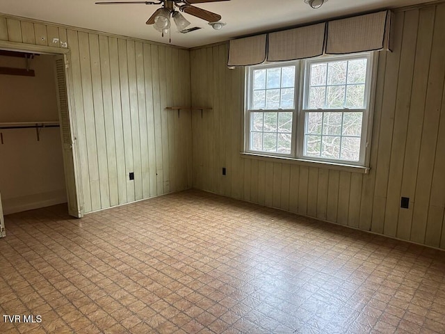 unfurnished bedroom featuring tile patterned floors, visible vents, wooden walls, and ceiling fan