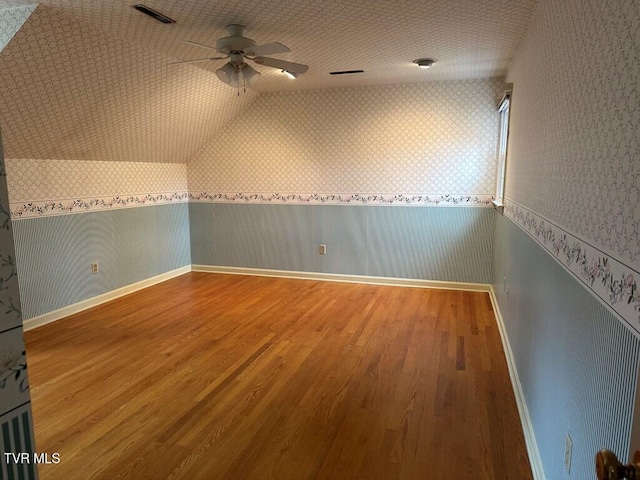additional living space featuring visible vents, wallpapered walls, lofted ceiling, and wood finished floors