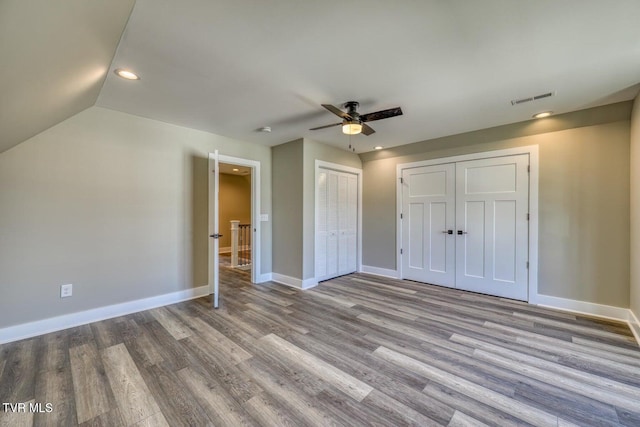 unfurnished bedroom featuring wood finished floors, baseboards, visible vents, and two closets