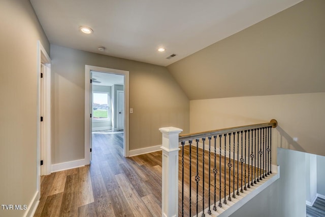 corridor with wood finished floors, baseboards, recessed lighting, vaulted ceiling, and an upstairs landing