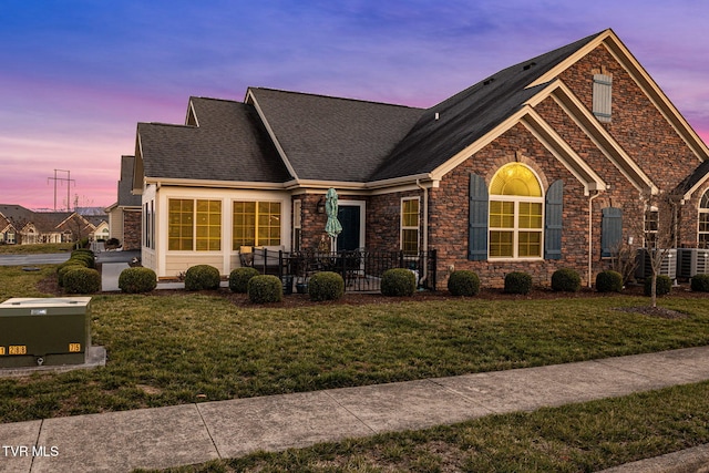 view of front of home with stone siding, a lawn, and roof with shingles