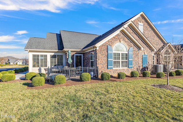 view of front facade featuring a front yard, cooling unit, stone siding, and a shingled roof