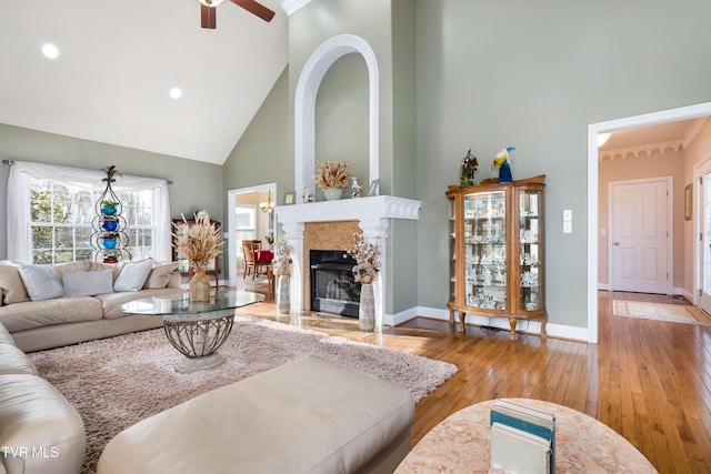 living room featuring baseboards, a fireplace, a high ceiling, hardwood / wood-style flooring, and a ceiling fan