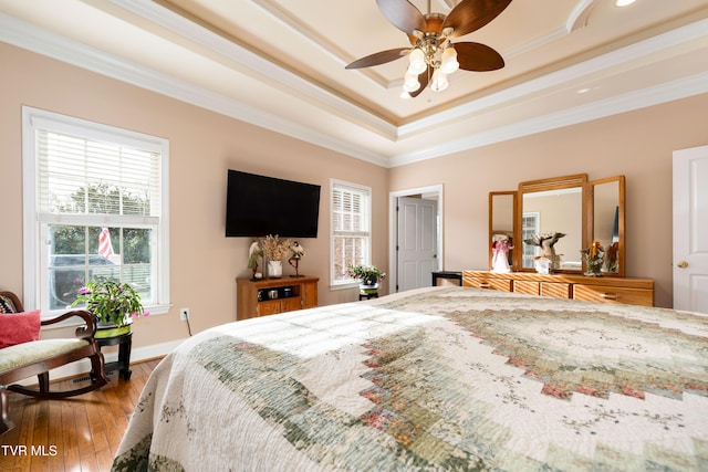 bedroom with hardwood / wood-style floors, baseboards, ceiling fan, ornamental molding, and a raised ceiling