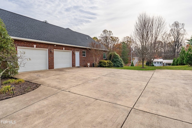 view of side of home with brick siding, driveway, a shingled roof, and an attached garage