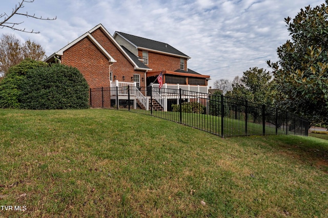 rear view of house featuring brick siding, a lawn, and fence